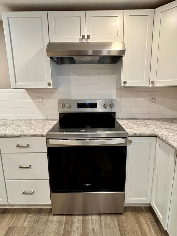 kitchen featuring stainless steel electric stove, tasteful backsplash, white cabinets, light stone countertops, and light hardwood / wood-style flooring