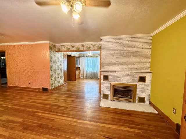 unfurnished living room with hardwood / wood-style flooring, a textured ceiling, a stone fireplace, and ornamental molding