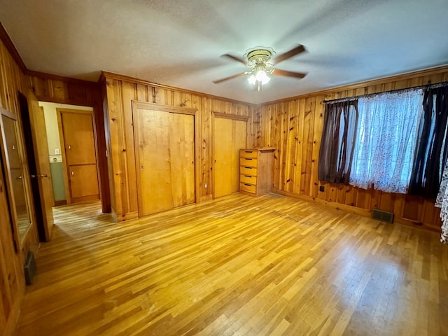 interior space featuring crown molding, light hardwood / wood-style floors, ceiling fan, multiple closets, and wooden walls