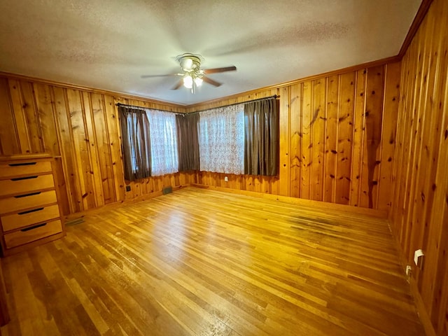 interior space with a textured ceiling, hardwood / wood-style floors, wooden walls, and ceiling fan