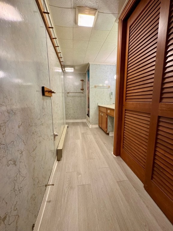 bathroom featuring light wood-type flooring, a baseboard heating unit, and a drop ceiling