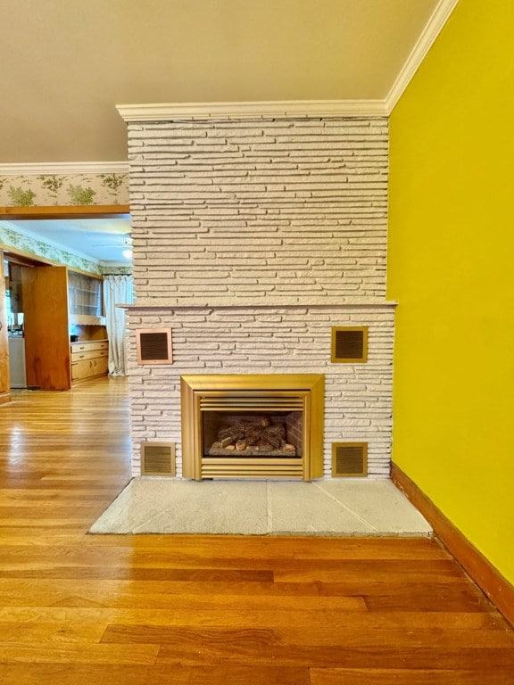 details featuring ornamental molding, a stone fireplace, and wood-type flooring