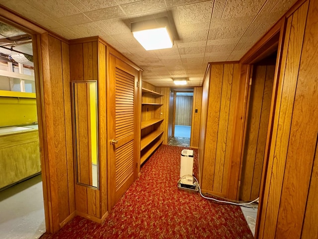 hallway featuring carpet and wood walls