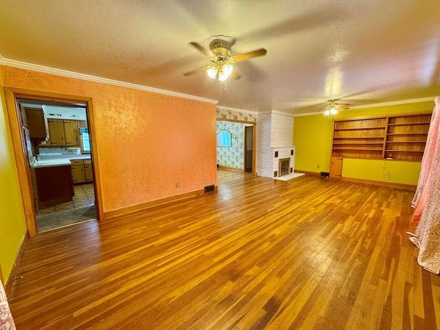 unfurnished living room with ceiling fan, ornamental molding, wood-type flooring, and a brick fireplace