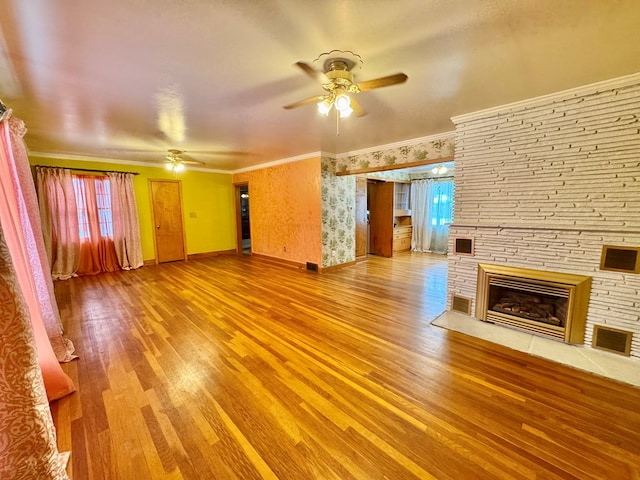 unfurnished living room featuring wood-type flooring, ceiling fan, crown molding, and a stone fireplace