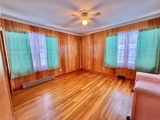 spare room with ornamental molding, light hardwood / wood-style floors, a baseboard heating unit, and wooden walls