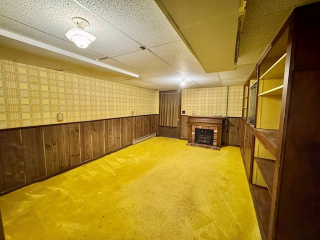 basement featuring baseboard heating, wooden walls, a paneled ceiling, and a fireplace