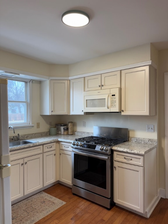 kitchen with sink, white appliances, light hardwood / wood-style floors, and white cabinets