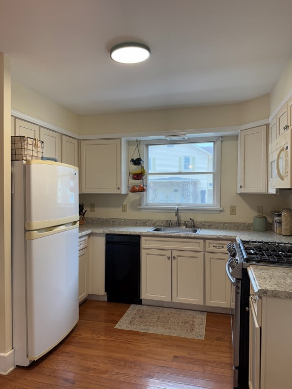 kitchen featuring sink, white appliances, hardwood / wood-style floors, and white cabinets