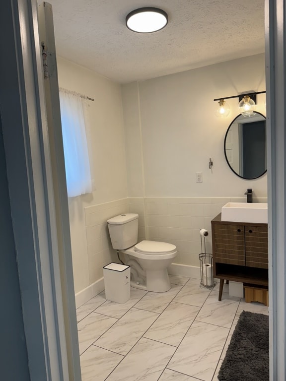 bathroom with vanity, tile walls, a textured ceiling, and toilet