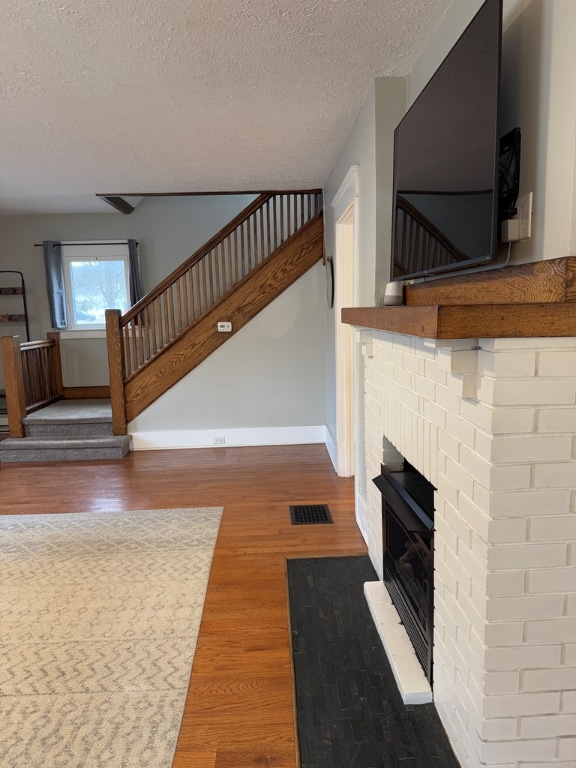 unfurnished living room featuring wood-type flooring, a brick fireplace, and a textured ceiling