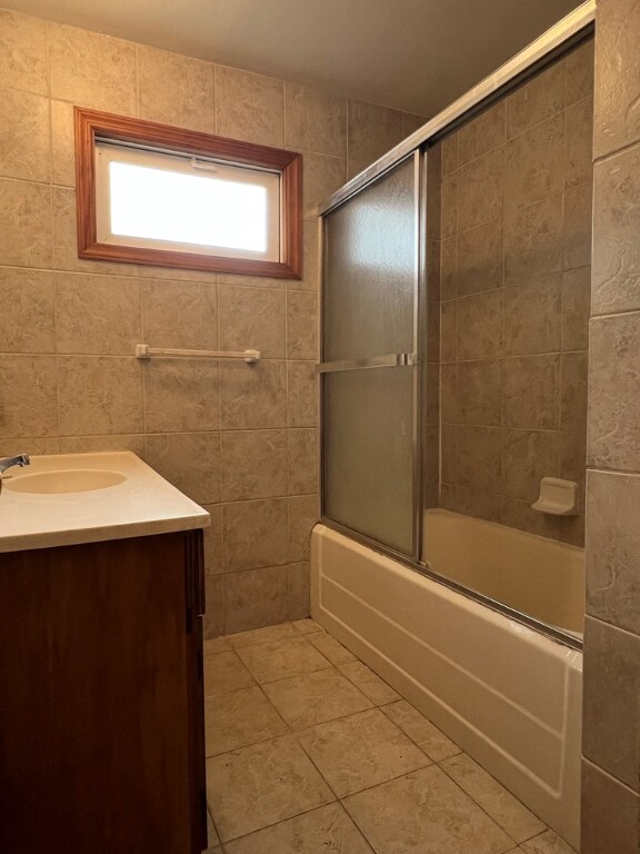 bathroom featuring vanity, bath / shower combo with glass door, tile patterned flooring, and tile walls