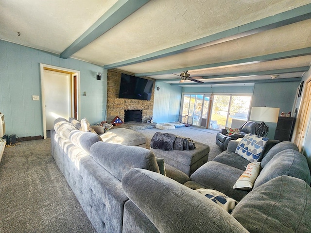 living room with beamed ceiling, ceiling fan, a stone fireplace, and carpet