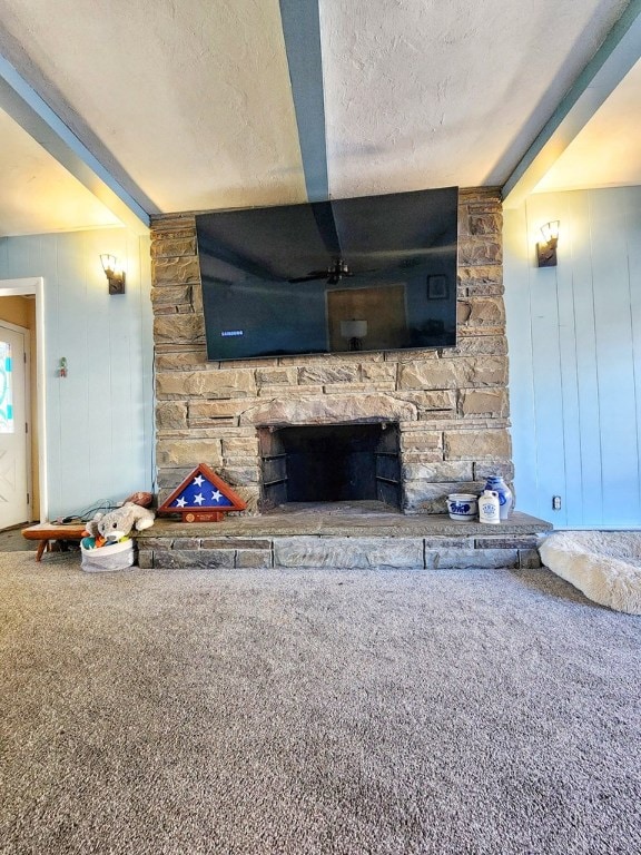 unfurnished living room featuring beam ceiling, a stone fireplace, carpet floors, and a textured ceiling