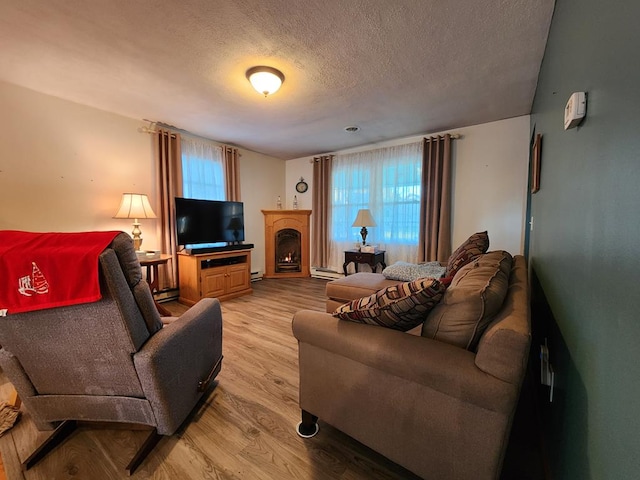 living room featuring baseboard heating, a textured ceiling, a healthy amount of sunlight, and light wood-type flooring