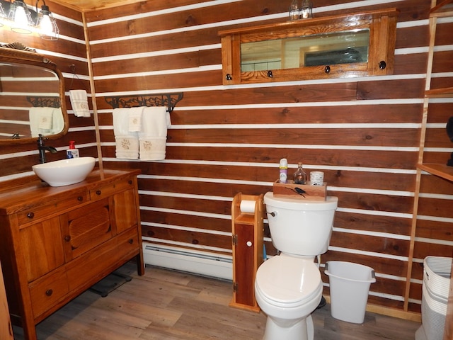 half bath featuring vanity, wooden walls, wood finished floors, toilet, and baseboard heating