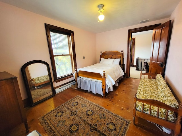 bedroom with a baseboard heating unit, visible vents, and hardwood / wood-style flooring