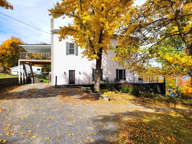 view of side of property featuring gravel driveway, a chimney, and a carport
