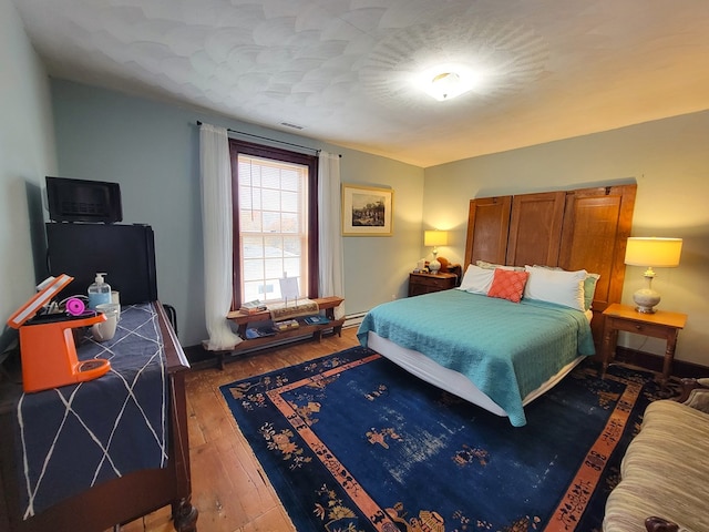 bedroom featuring hardwood / wood-style floors, baseboard heating, visible vents, and baseboards