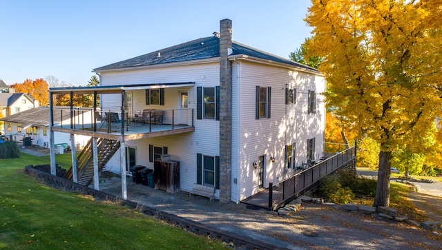 rear view of house featuring stairs, a chimney, a lawn, and a wooden deck