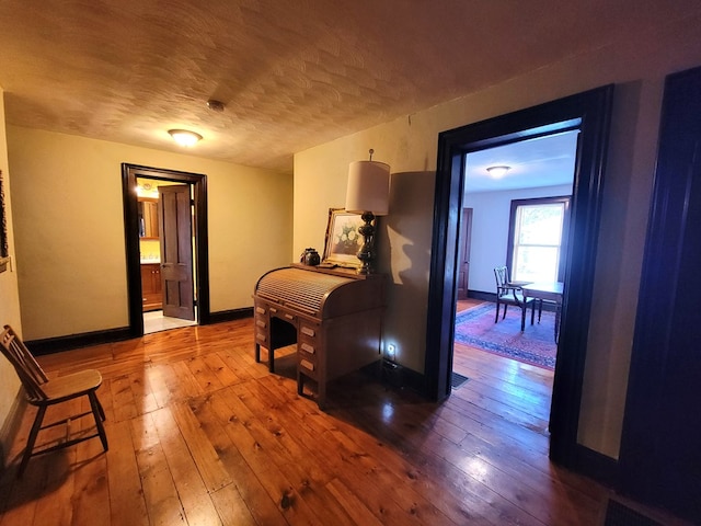 corridor featuring a textured ceiling, visible vents, hardwood / wood-style flooring, and baseboards