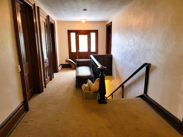 hall featuring baseboards, light colored carpet, and a textured wall
