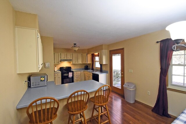 kitchen with sink, a kitchen breakfast bar, dark hardwood / wood-style flooring, kitchen peninsula, and black appliances