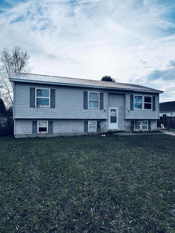 raised ranch featuring a front lawn, fence, and metal roof