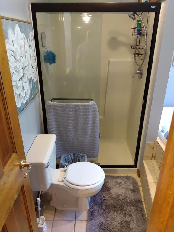 bathroom with tile patterned floors, toilet, and a shower with door