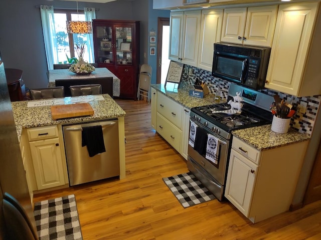 kitchen featuring stainless steel appliances, tasteful backsplash, light stone counters, light hardwood / wood-style floors, and decorative light fixtures