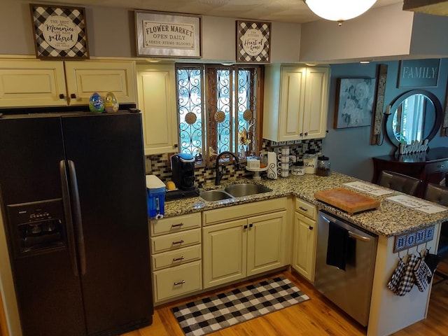 kitchen featuring sink, light stone counters, black fridge with ice dispenser, stainless steel dishwasher, and light wood-type flooring