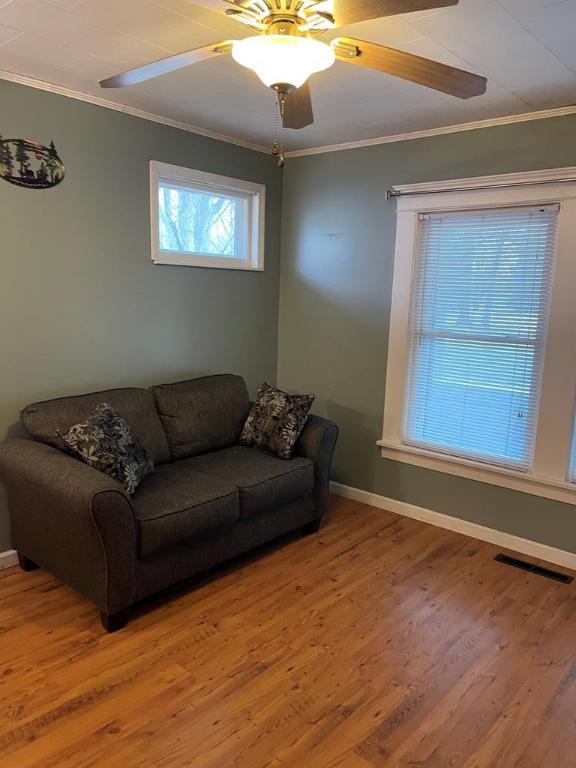 living room with hardwood / wood-style flooring, ornamental molding, and ceiling fan