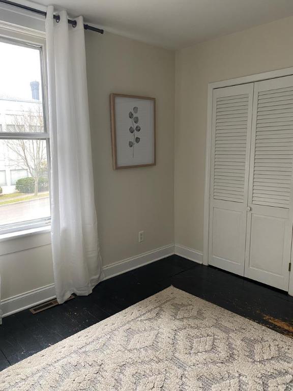 unfurnished bedroom with multiple windows, a closet, and dark hardwood / wood-style floors