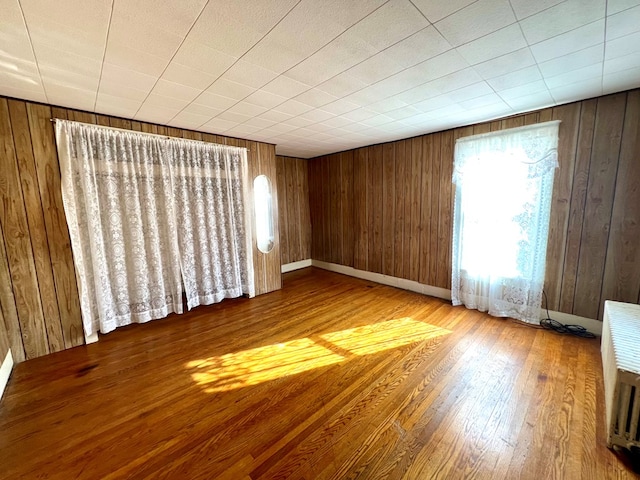 empty room with heating unit, hardwood / wood-style flooring, and wooden walls