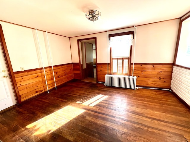 unfurnished room with radiator, dark hardwood / wood-style flooring, and wood walls