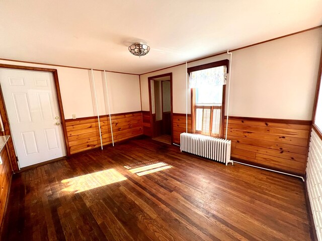 empty room featuring wooden walls, radiator heating unit, and dark hardwood / wood-style floors