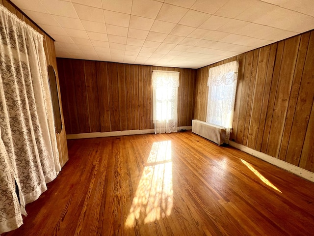 empty room with hardwood / wood-style flooring, radiator heating unit, and wood walls