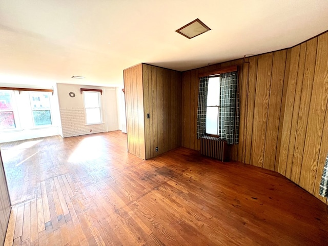 empty room featuring hardwood / wood-style flooring, radiator, and wood walls