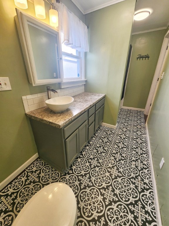 bathroom with tasteful backsplash, tile patterned flooring, vanity, toilet, and crown molding