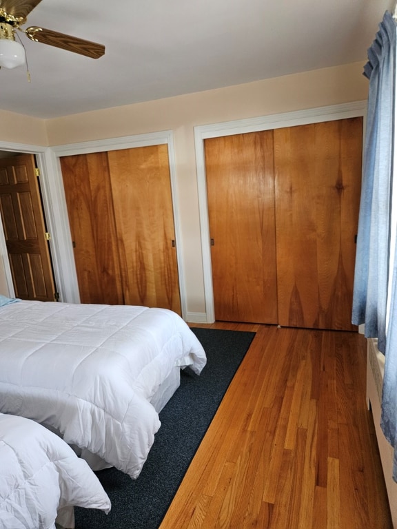 bedroom with multiple closets, hardwood / wood-style flooring, and ceiling fan