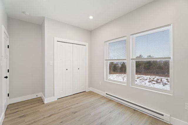 unfurnished bedroom with a baseboard heating unit, light hardwood / wood-style floors, and a closet