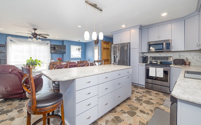 kitchen featuring gray cabinetry, decorative light fixtures, a kitchen island, stainless steel appliances, and decorative backsplash