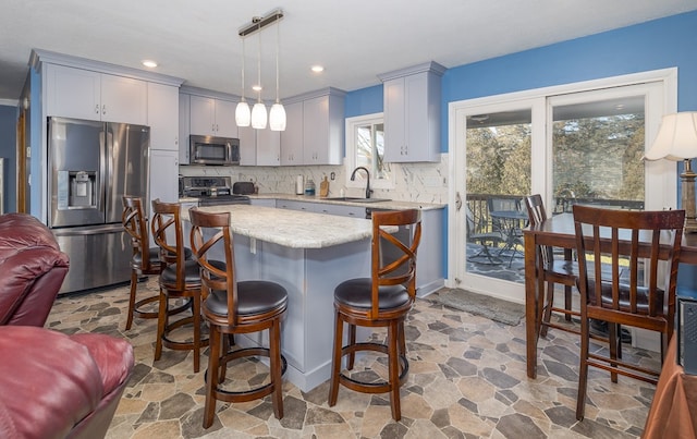 kitchen with sink, appliances with stainless steel finishes, backsplash, a center island, and decorative light fixtures