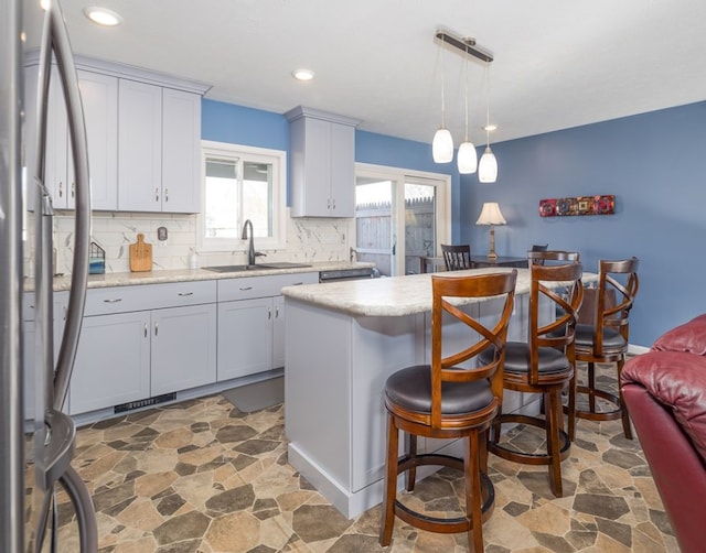 kitchen featuring sink, stainless steel refrigerator, hanging light fixtures, backsplash, and a center island