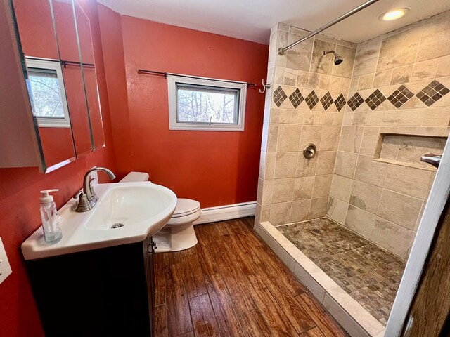 bathroom with a tile shower, wood-type flooring, a baseboard radiator, vanity, and toilet