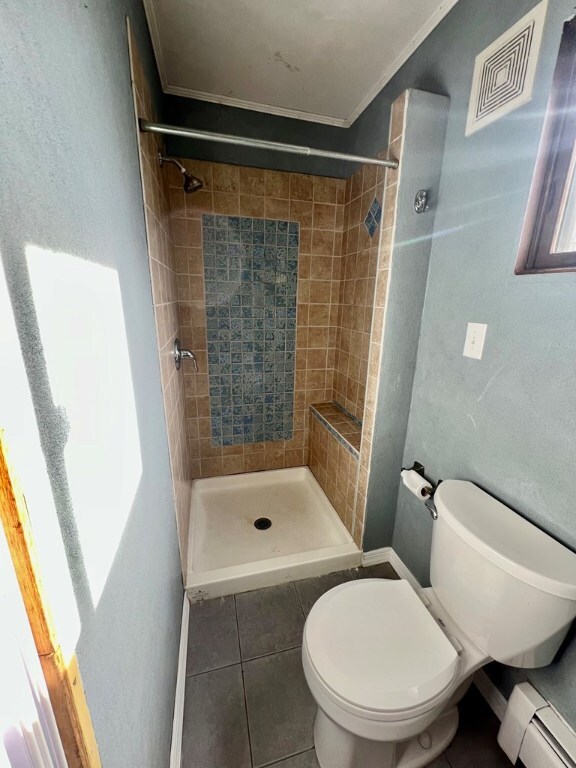 bathroom featuring toilet, a tile shower, ornamental molding, tile patterned flooring, and a baseboard heating unit