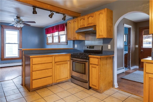 kitchen featuring arched walkways, dark countertops, baseboard heating, under cabinet range hood, and gas stove