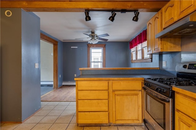 kitchen with light tile patterned floors, stainless steel gas range oven, a baseboard radiator, under cabinet range hood, and dark countertops