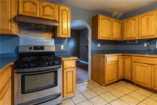 kitchen with light tile patterned floors, dark countertops, gas range, under cabinet range hood, and a sink