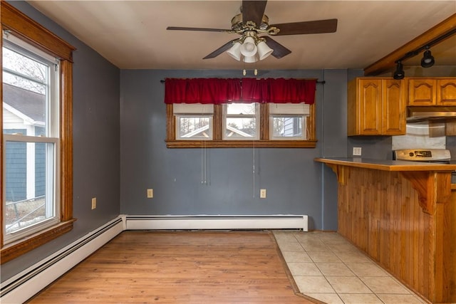 kitchen with brown cabinetry, a peninsula, light countertops, under cabinet range hood, and a baseboard heating unit